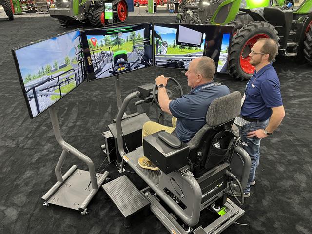 DTN/Progressive Farmer Senior Editor Dan Miller (left) leaves the yard in Fendt&#039;s Rogator 900 series sprayer simulator. He missed the tanks and vehicles coming down the highway, but soon crushed a stop sign, twice. (Photo courtesy of Fendt)