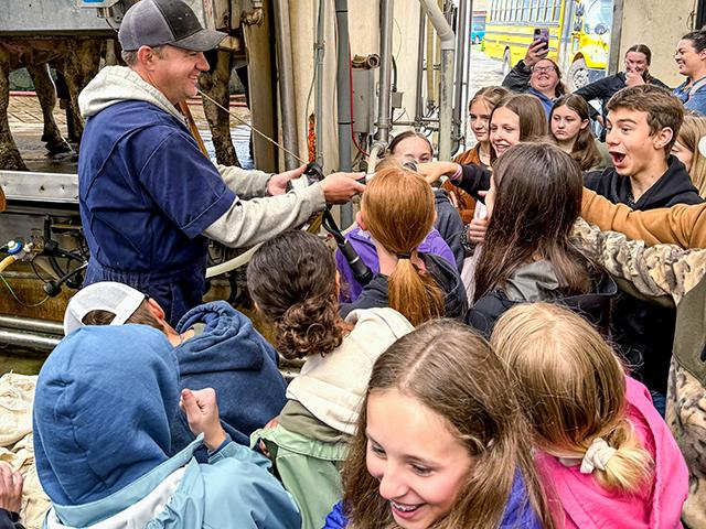Marinus Noordam of AJ Dairy in Mount Angel, Oregon, hosts seventh-grade students on a field trip to learn about all aspects of dairy farming from raising calves to how milk is collected and processed. Here he allows the students from Victor Point School in Silverton, Oregon, to feel the gentle vacuum suction pulsation inside the shell of the milking machine before the students see how it is used on cows in the milking parlor. (Photo courtesy of Oregon Aglink)