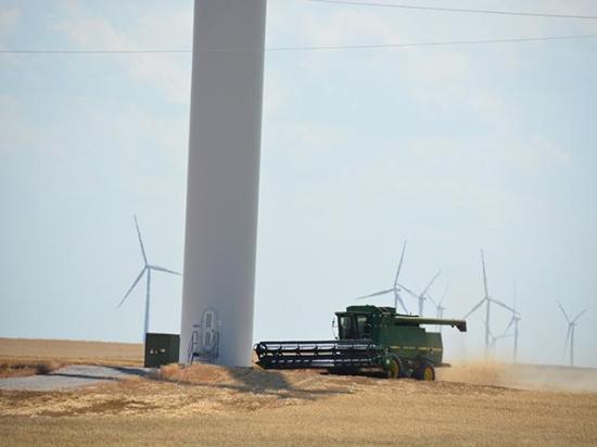 An Oklahoma farmer harvests wheat around wind turbines in western Oklahoma. The Inflation Reduction Act will drive more incentives to increase renewable energy such as wind and solar production in rural America. (DTN photo by Chris Clayton) 