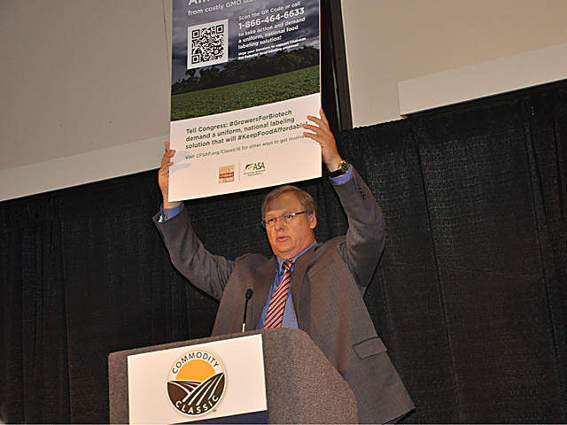 Wade Cowan, a Texas farmer and chairman of the American Soybean Association, holds up a sign during Commodity Classic showing how farmers can reach senators to talk about the biotech labeling push in the U.S. Senate. (DTN photo by Chris Clayton)