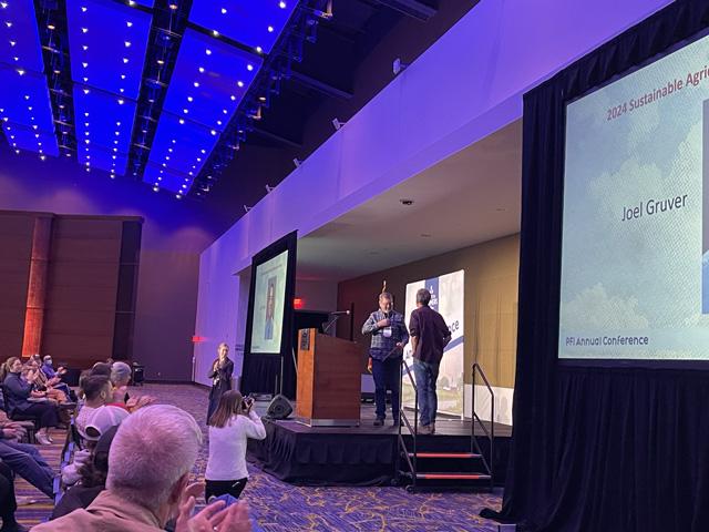 Dr. Joel Gruver, on stage at right, takes the stage to receive his 2024 Sustainable Agriculture Award from Practical Farmers of Iowa board member Mark Quee at the annual conference on Jan. 19, 2024. (DTN photo by Susan Payne)
