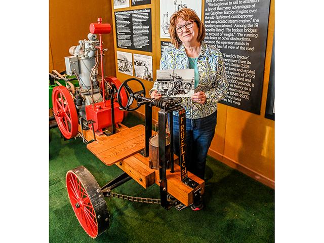 Denise Schutte, executive director of the Froelich Foundation for the Preservation of Farm Tractor History Inc., stands next to a half-scale replica of the first gasoline-powered tractor to go forward and backward and holds a photo of the original machine built in 1892. Froelich, Iowa, is home to the Froelich Tractor and 1890s Village Museum. (Matthew Wilde)