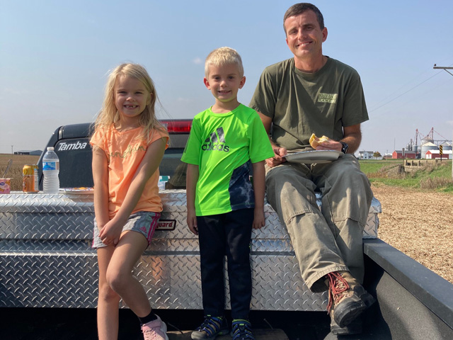 A quick meal in the field is more than food, it unites families. Eleanor, Luke and Ryan Frieders take a moment during harvest to share the comfort of a meal. (Photo courtesy of Deanne Frieders)