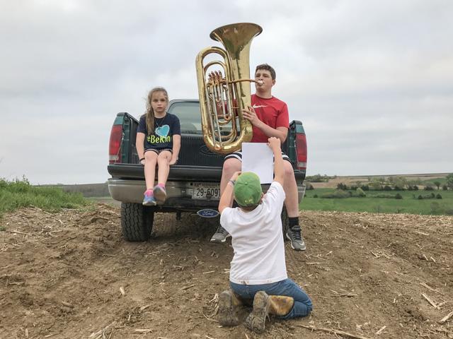 Kyle Quinn, 15, plays his tuba from a high spot on the Quinn farm in order to get a strong enough mobile phone signal to send his performance to his band teacher. Brother Burke, 10, holds the music and sister Ella, 8, listens. (DTN photo by Russ Quinn.)