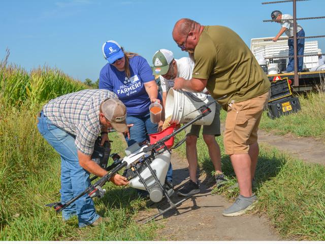 Sarah Carlson, second from left, of Practical Farmers of Iowa, and landowner Lee Tesdell, third from left, help fill a drone with cover crop seed late last summer during a conservation field day on his farm near Slater, Iowa. Tesdell, along with local conservation groups, showed off various soil health and water quality practices on his land, including how drones can be effective tools applying cover crop seed in standing corn. (DTN photo by Matthew Wilde)