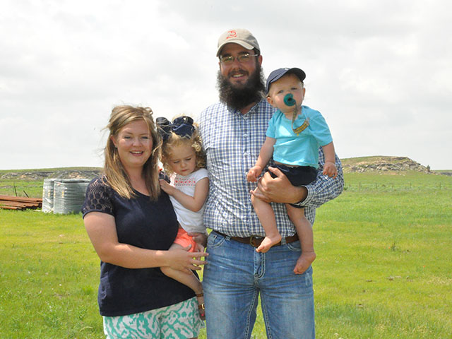 Chaz and Lori Rutledge&#039;s Texas ranch survived the March wildfires when winds shifted in time to prevent the fire from broaching the fence line behind them. Also pictured are their children, Maddy, 2, and Hudson, 1. (DTN photo by Todd Neeley)
