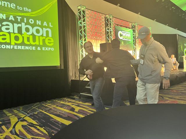 A protester is escorted out of a carbon capture conference Tuesday in Des Moines. Representatives from three carbon pipeline projects tied to Iowa ethanol plants were highlighting the ability to lower the carbon-intensity score of ethanol plants. (DTN photo by Chris Clayton) 