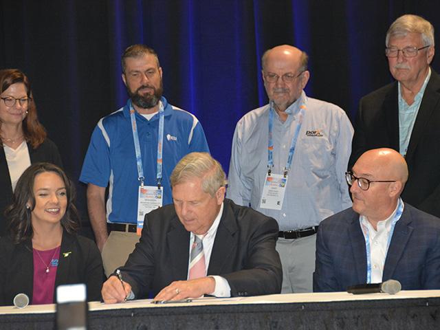 Agriculture Secretary Tom Vilsack signs a memorandum of understanding to fund the Farmers for Soil Health partnerships while surrounded by representatives from the farm associations and checkoff organizations that are part of the pilot project. The group will use incentives to help encourage farmers to grow cover crops in 20 states. (DTN photo by Chris Clayton) 